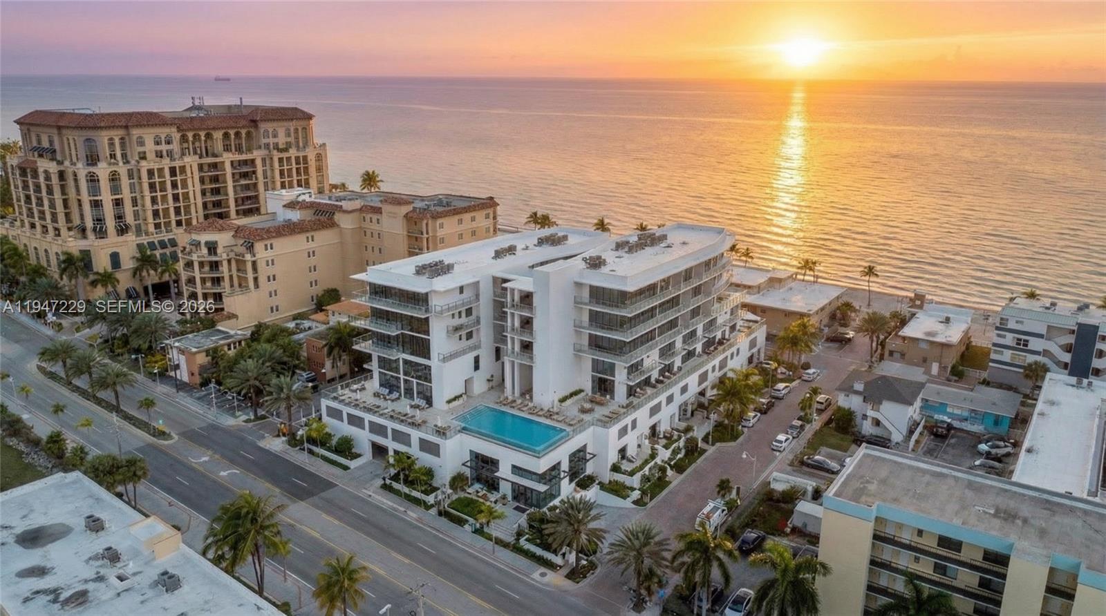 An aerial view shows a modern white beachfront building with a rooftop pool at sunset — 3319 N Ocean Drive, Hollywood FL 33019, HOLLYWOOD, FL