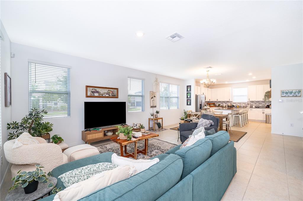 An open-concept living room features a blue sectional sofa, a television, and a kitchen area — 2929 VOYAGER AVENUE, ST CLOUD, FL