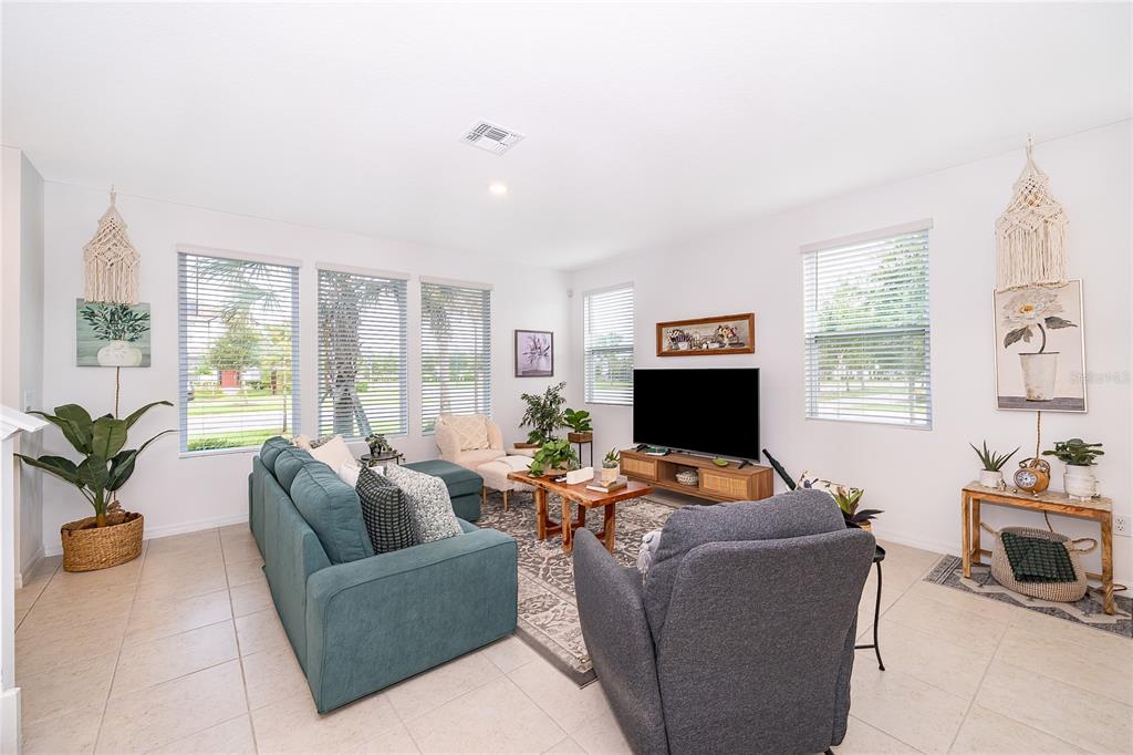 A bright living room features a blue sectional sofa, a television, and large windows — 2929 VOYAGER AVENUE, ST CLOUD, FL