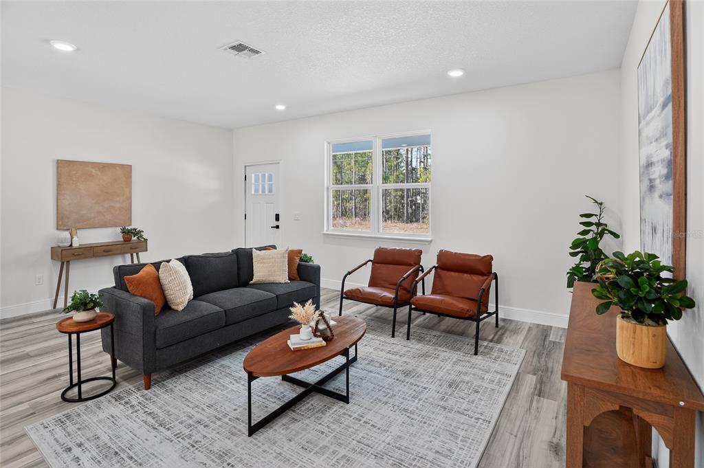 A living room features a gray sofa, two leather chairs, a coffee table, and wood-look flooring — 7945 N JANEAUX DRIVE, CITRUS SPRINGS, FL