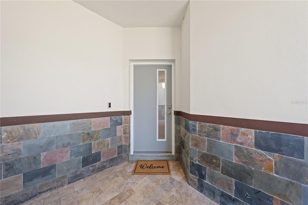 A gray front door with a vertical window sits in a stone-tiled entryway — 1935 GREENBRIAR TERRACE, DAVENPORT, FL