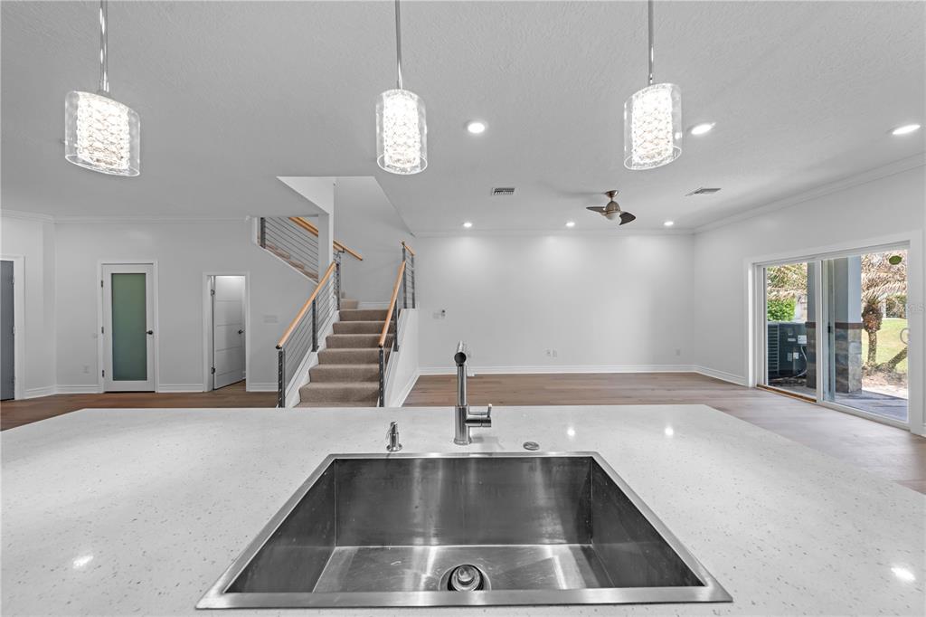 A kitchen island with a stainless steel sink overlooks an open living area and staircase — 1935 GREENBRIAR TERRACE, DAVENPORT, FL