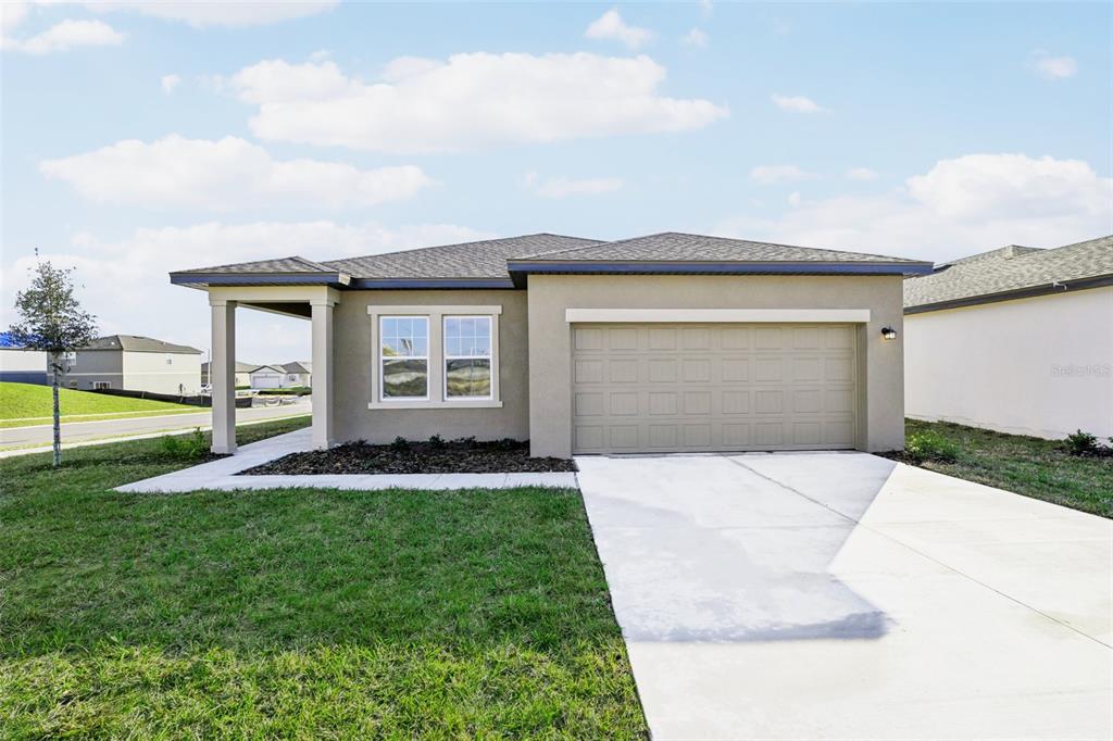 A single-story house with a beige stucco exterior, a two-car garage, and a covered entryway — 3207 CARNATION AVENUE, LAKE HAMILTON, FL