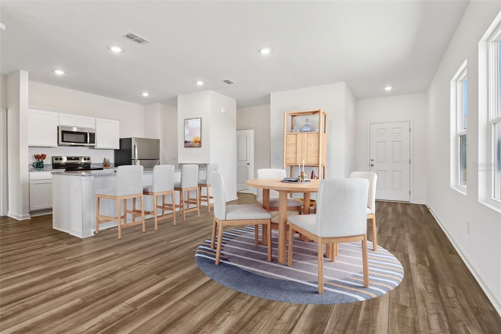 An open-concept kitchen and dining area features light wood flooring, white cabinetry, and neutral furniture — 3207 CARNATION AVENUE, LAKE HAMILTON, FL