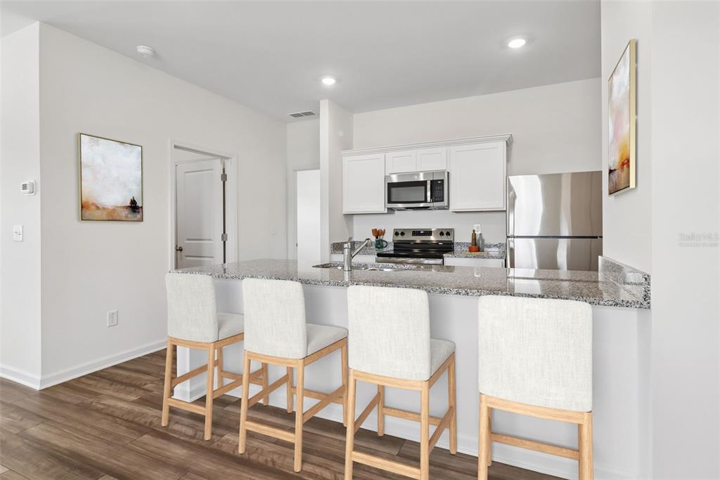 A kitchen features a granite breakfast bar with four stools and stainless steel appliances — 3207 CARNATION AVENUE, LAKE HAMILTON, FL