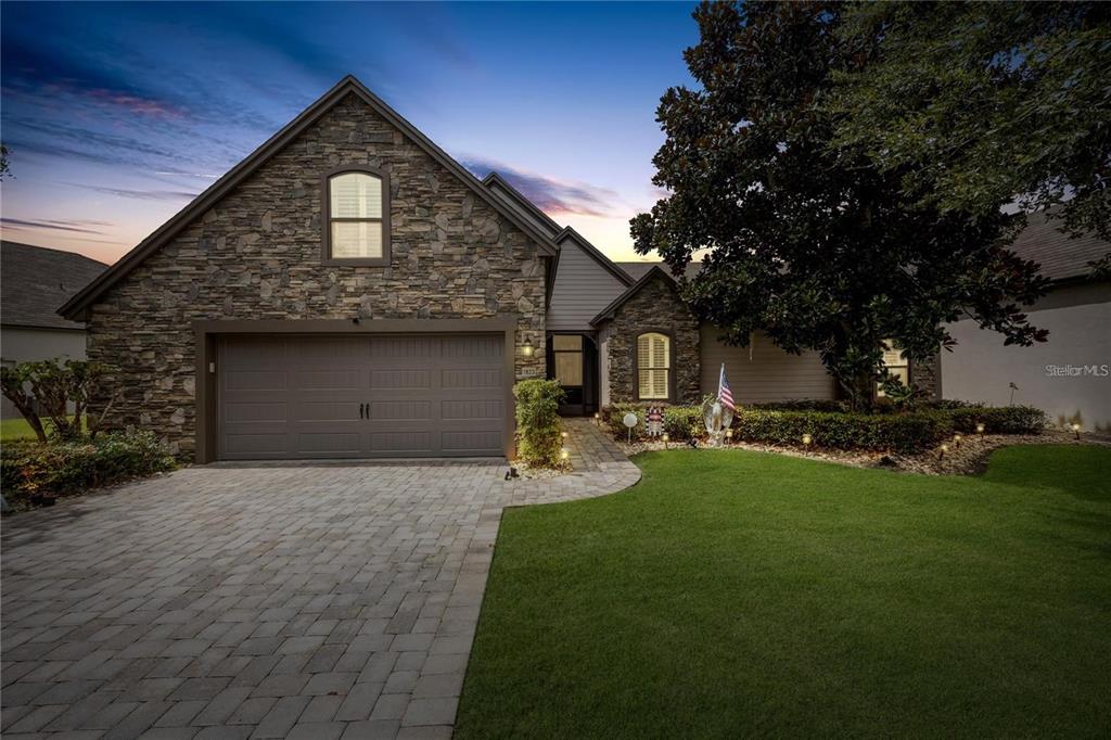 A stone-front house features a paved driveway, a two-car garage, and a manicured lawn — 1923 BANNING BEACH ROAD, TAVARES, FL
