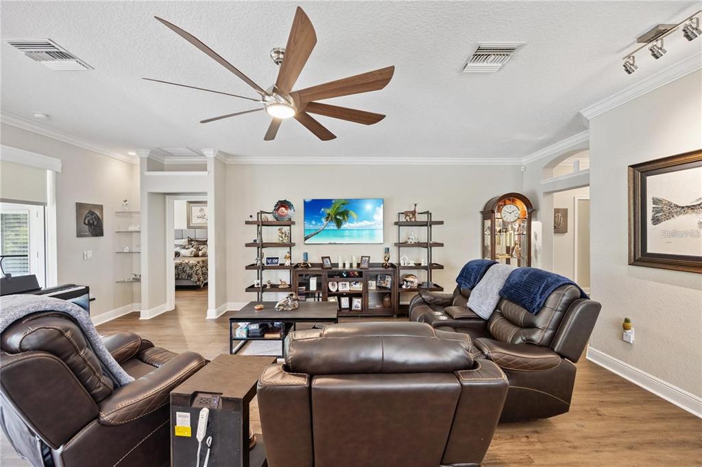 A living room features leather recliners, a television, shelving, and a wooden ceiling fan — 1923 BANNING BEACH ROAD, TAVARES, FL