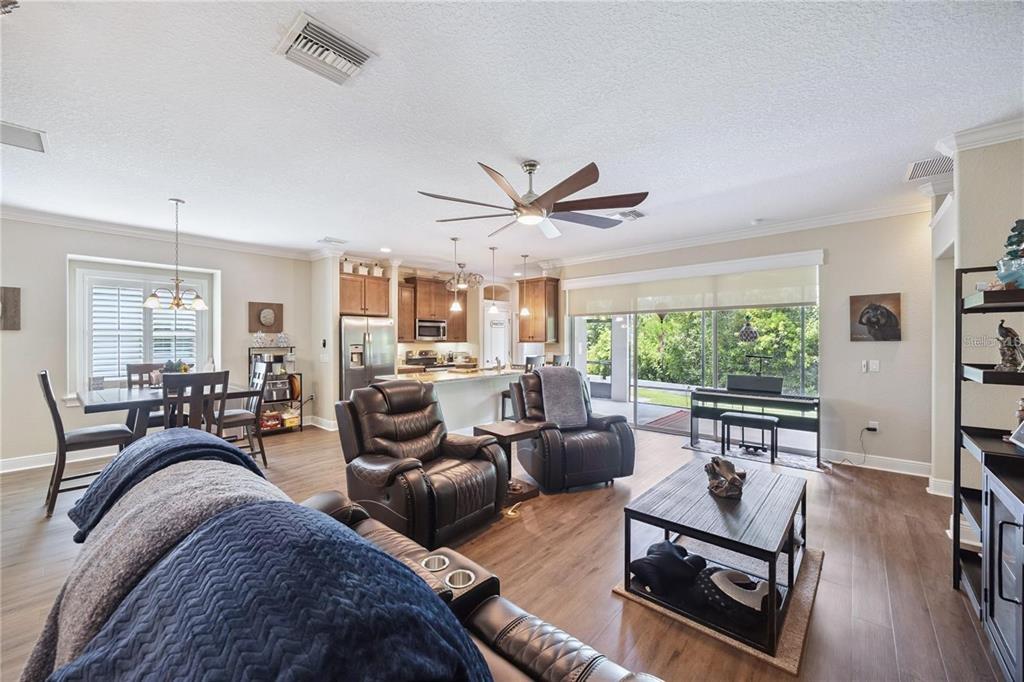 An open-concept living room and kitchen featuring wood-look flooring and a large sliding glass door — 1923 BANNING BEACH ROAD, TAVARES, FL