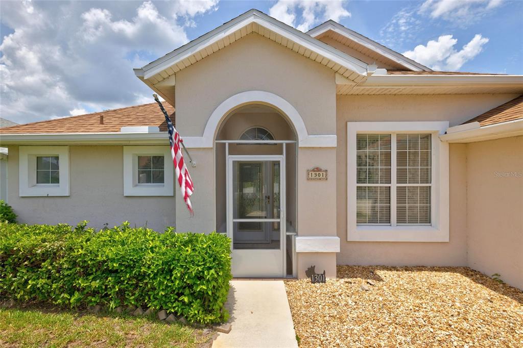 The exterior of a single-story house features a tan stucco facade, a screened entryway, and landscaping — 1301 FLAGSHIP COURT, ST AUGUSTINE, FL