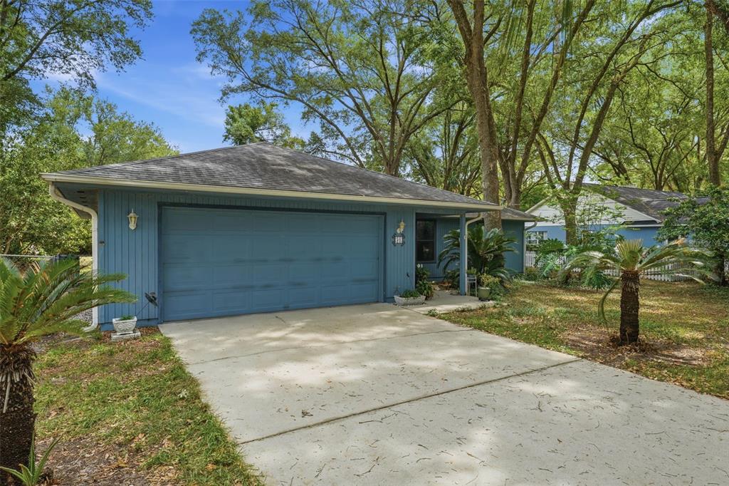 A blue single-story house with a two-car garage and a concrete driveway under large trees — 31 ALMOND PASS DRIVE, OCALA, FL