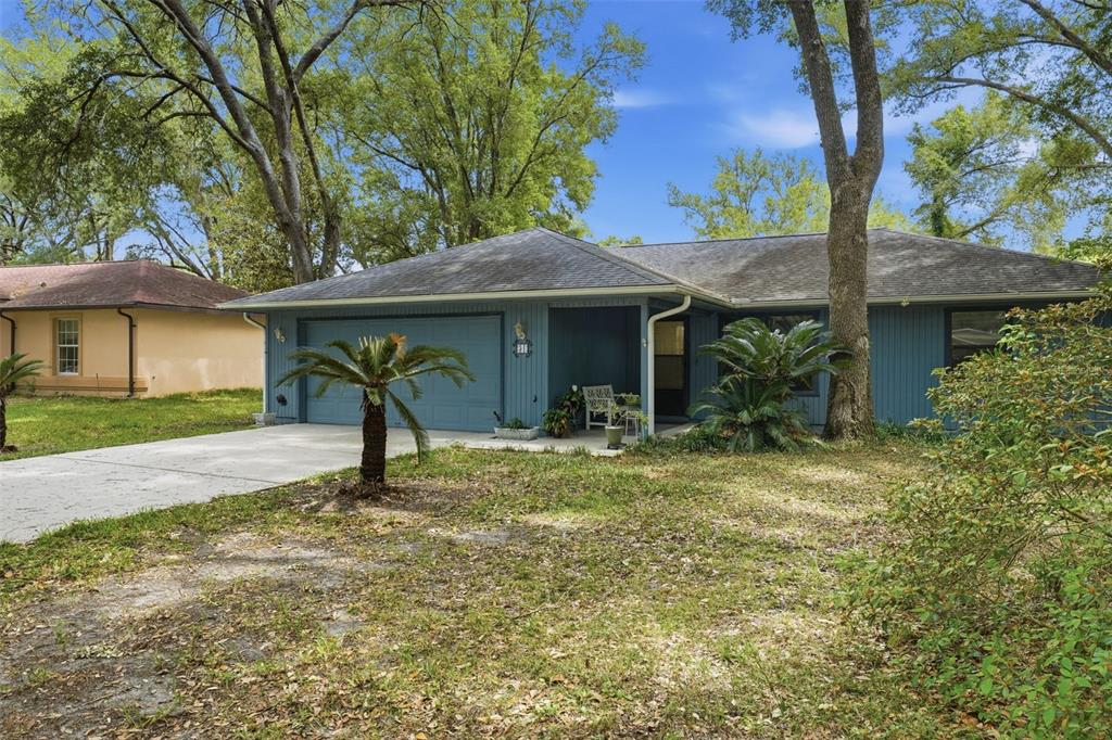 A blue, single-story house with a two-car garage and a front yard with trees — 31 ALMOND PASS DRIVE, OCALA, FL