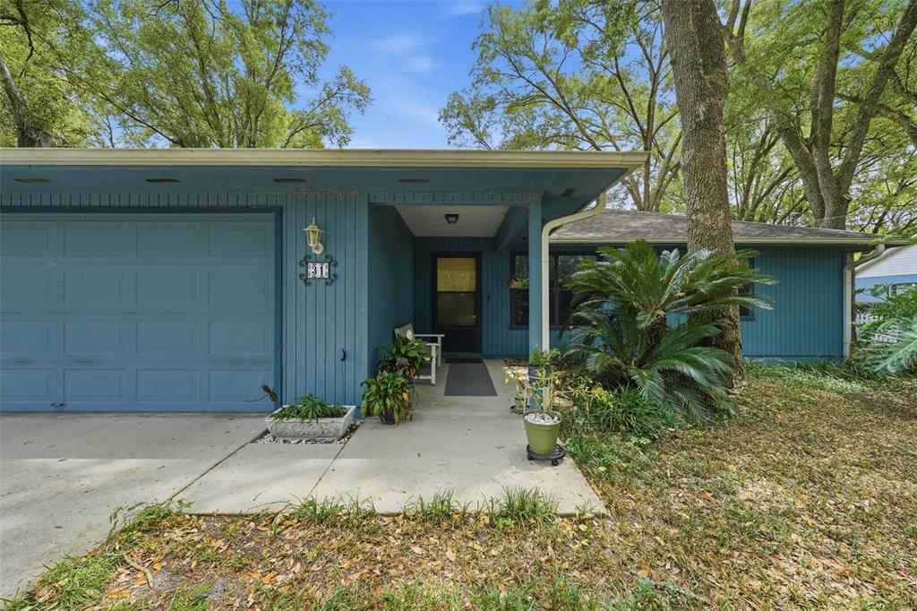 A blue house exterior features a single-car garage, a covered entryway, and mature landscaping — 31 ALMOND PASS DRIVE, OCALA, FL