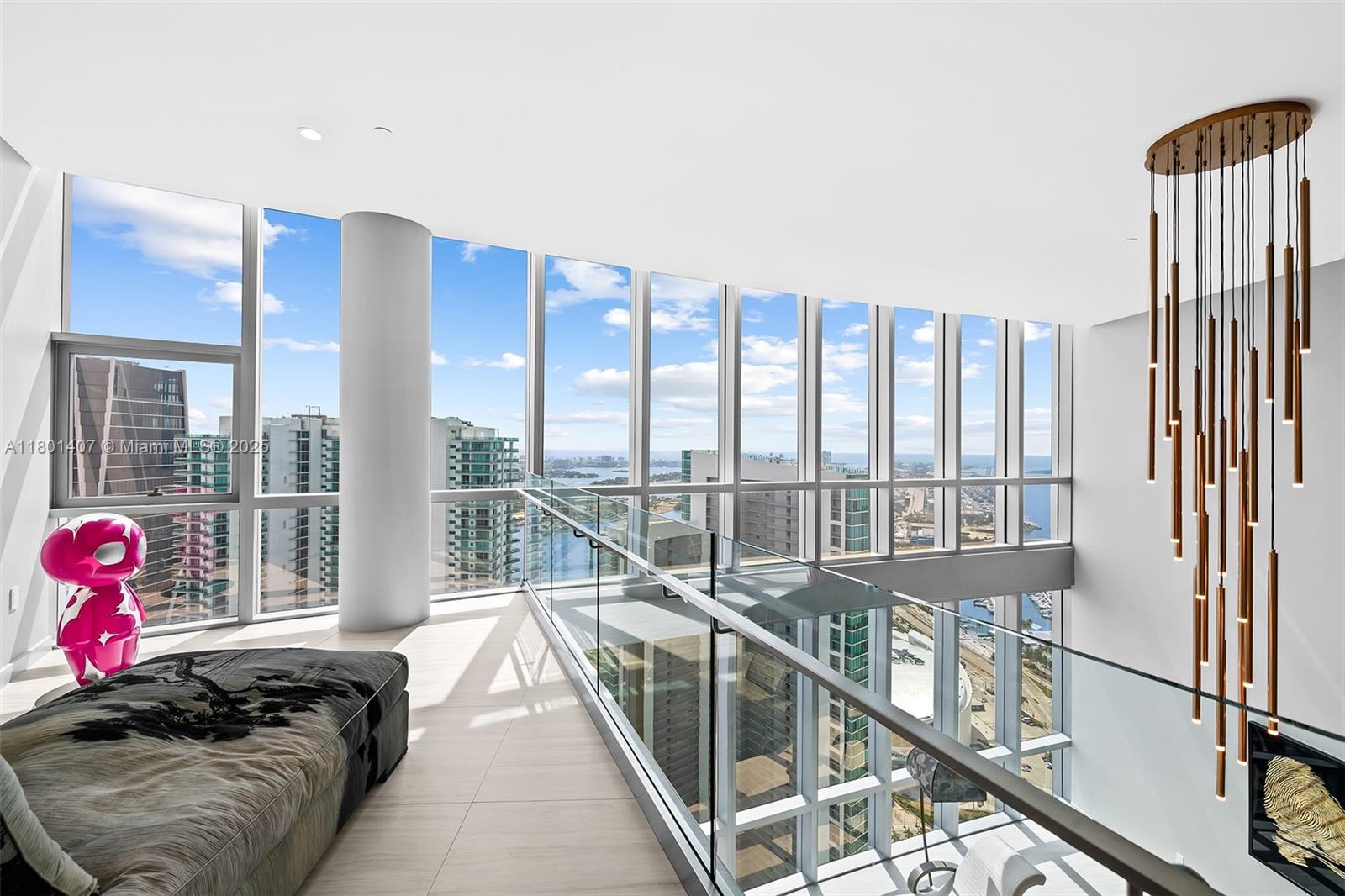 A modern lofted living area features floor-to-ceiling windows, a glass railing, and a hanging chandelier — 851 NE 1st Ave # 5401, Miami FL 33132, MIAMI, FL