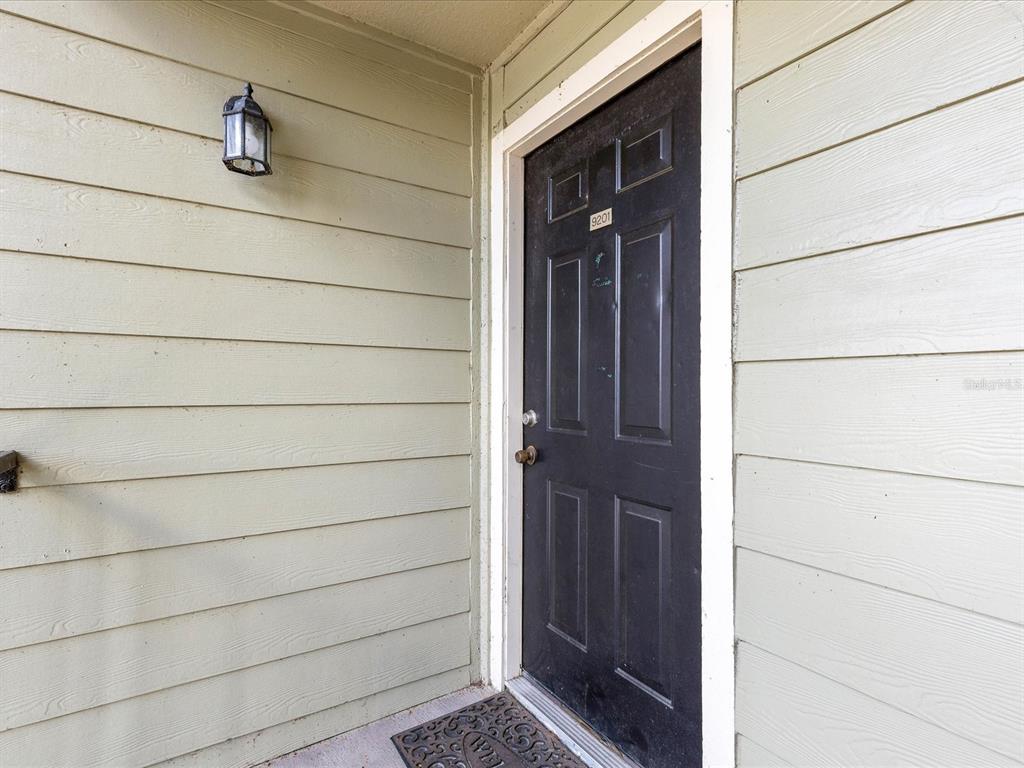 A black front door with a house number is set into light green horizontal siding — 2550 N ALAFAYA TRAIL UNIT 9201, ORLANDO, FL