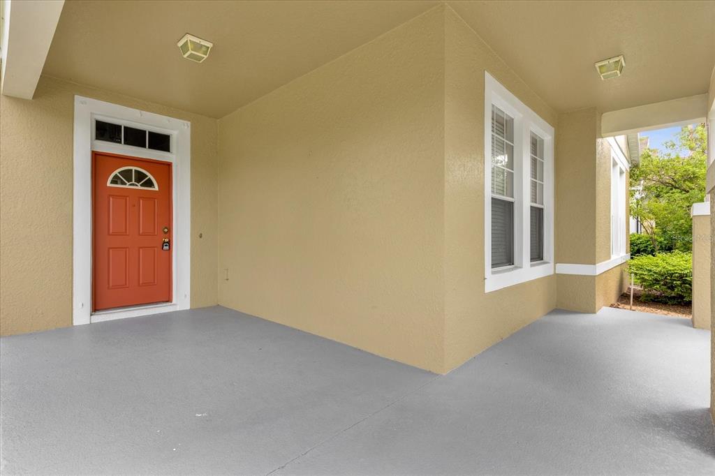 A covered porch features a red front door, light-colored walls, and a gray concrete floor — 14217  BRIDGEWATER CROSSINGS BOULEVARD, WINDERMERE, FL
