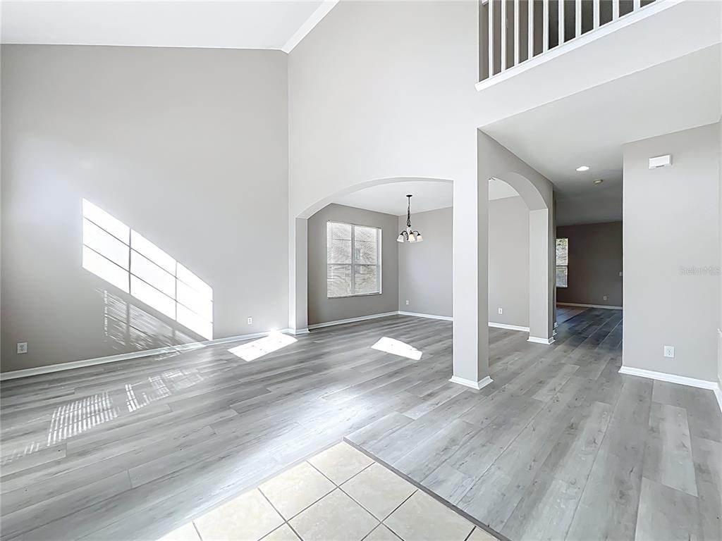 A bright living and dining area features high ceilings, gray wood-look flooring, and arched openings — 33411 TERRAGONA DRIVE, SORRENTO, FL