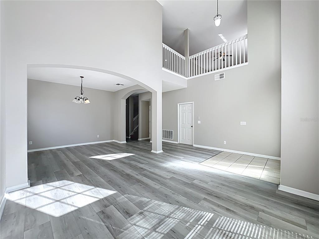 An open-concept living area features gray wood-look flooring, high ceilings, and a white balcony railing — 33411 TERRAGONA DRIVE, SORRENTO, FL