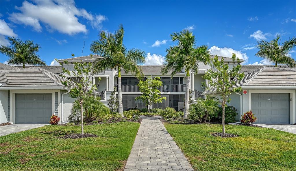 A two-story residential building with two garages, palm trees, and a stone walkway — 12390 WELLEN GOLF STREET UNIT 107, VENICE, FL