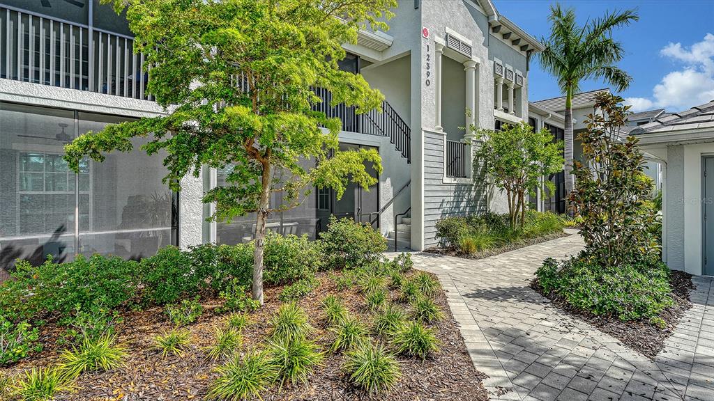 A paved walkway leads to the entrance of a multi-story residential building with screened balconies — 12390 WELLEN GOLF STREET UNIT 107, VENICE, FL