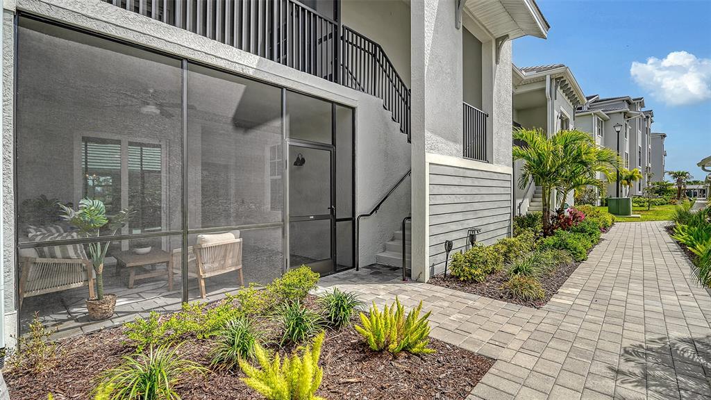 A ground-floor screened-in patio with outdoor furniture sits beside a paved walkway and landscaping — 12390 WELLEN GOLF STREET UNIT 107, VENICE, FL