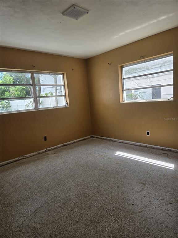 An empty bedroom features tan walls, a speckled floor, and two windows with metal frames — 1216 FRANKLIN CIRCLE, CLEARWATER, FL