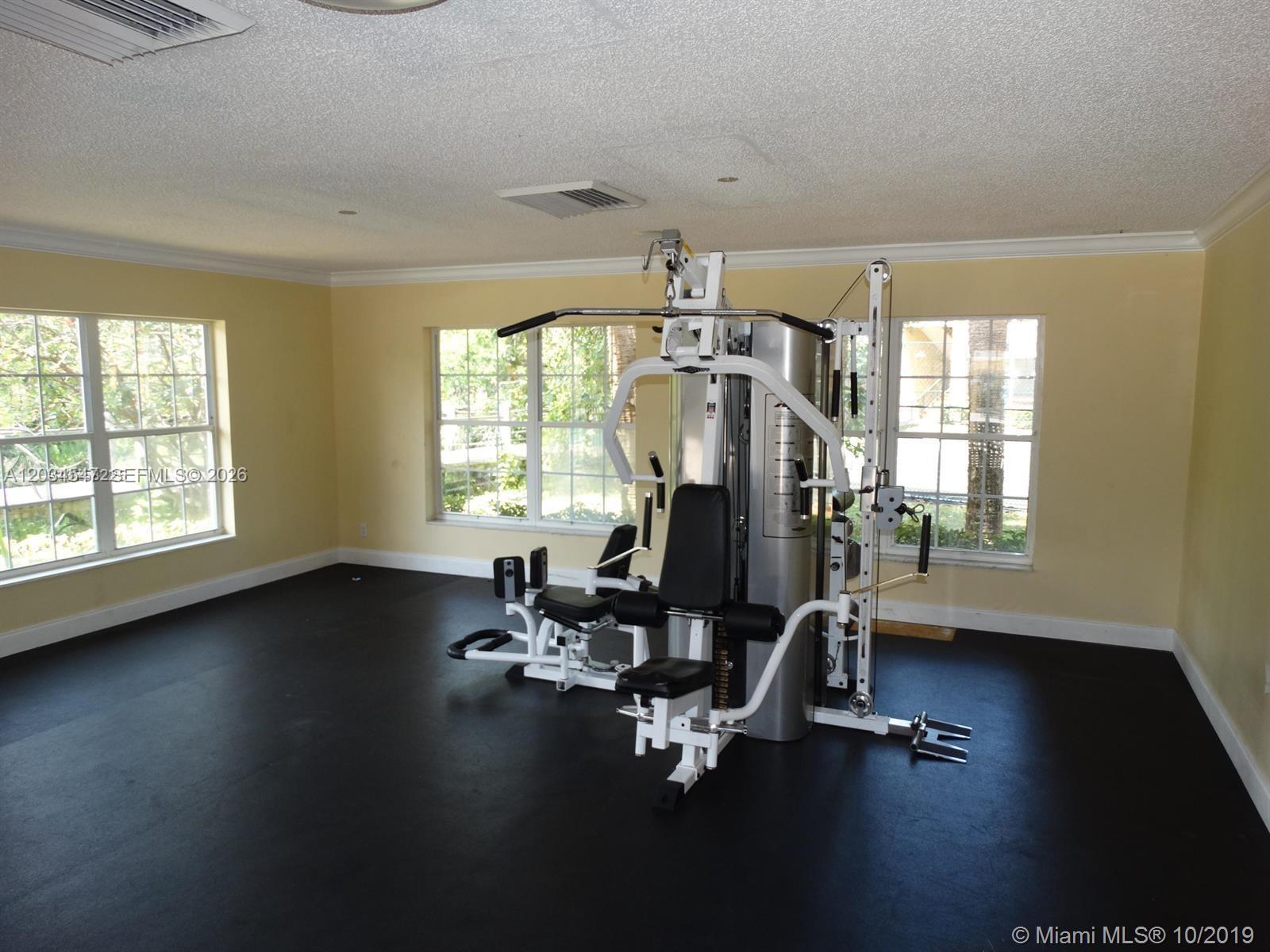 A home gym features a multi-station exercise machine on black flooring with yellow walls — 4015 W Mcnab Rd # D210, Pompano Beach FL 33069, POMPANO BEACH, FL
