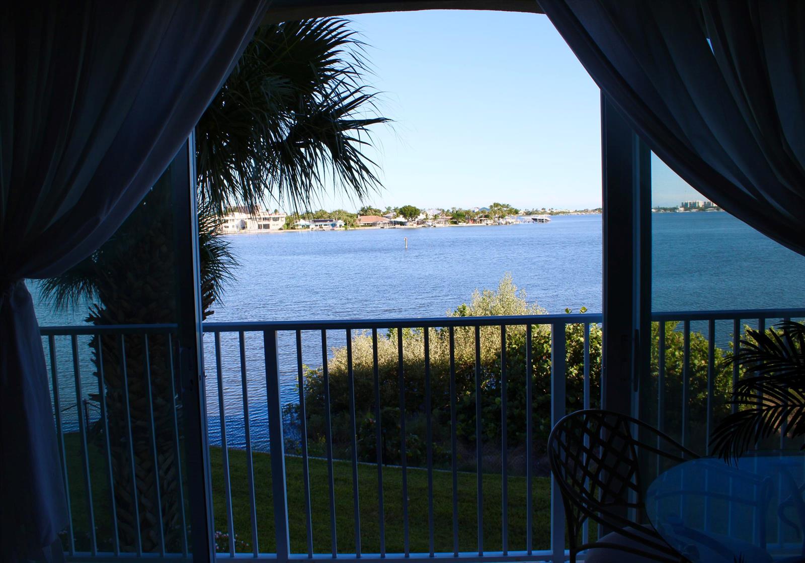 A view of a waterfront bay from a balcony framed by indoor curtains — 3 E Harbour Isle Drive E # 204, Fort Pierce FL 34949, FORT PIERCE, FL