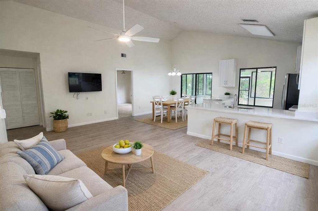 An open-concept living and dining area with light wood flooring, white walls, and a kitchen — 114 SPREADING OAK COURT, SANFORD, FL