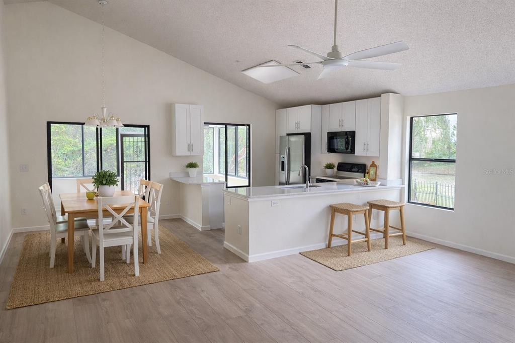 A bright kitchen and dining area features white cabinets, a breakfast bar, and vaulted ceilings — 114 SPREADING OAK COURT, SANFORD, FL