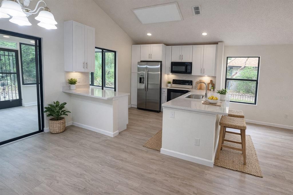 A modern kitchen features white cabinets, stainless steel appliances, a center island, and light flooring — 114 SPREADING OAK COURT, SANFORD, FL