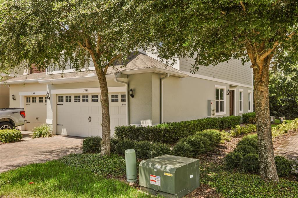 A two-story townhouse exterior features a white garage, light-colored siding, and mature trees in front — 2340 BRITWELL PLACE, SANFORD, FL