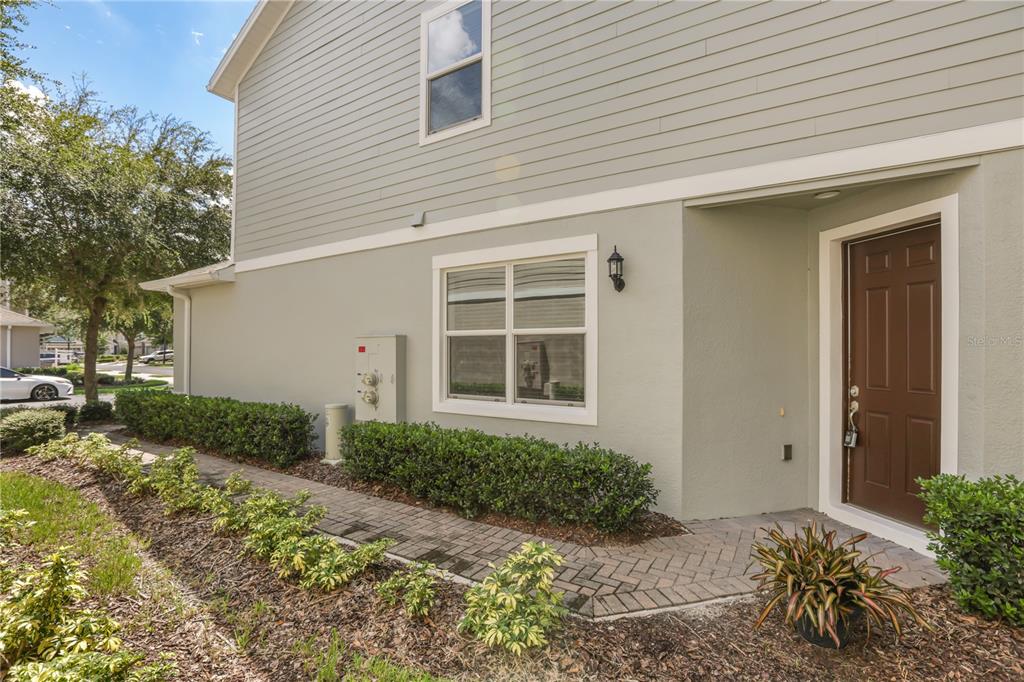 A side view of a house exterior featuring a brown door, window, and paved walkway — 2340 BRITWELL PLACE, SANFORD, FL