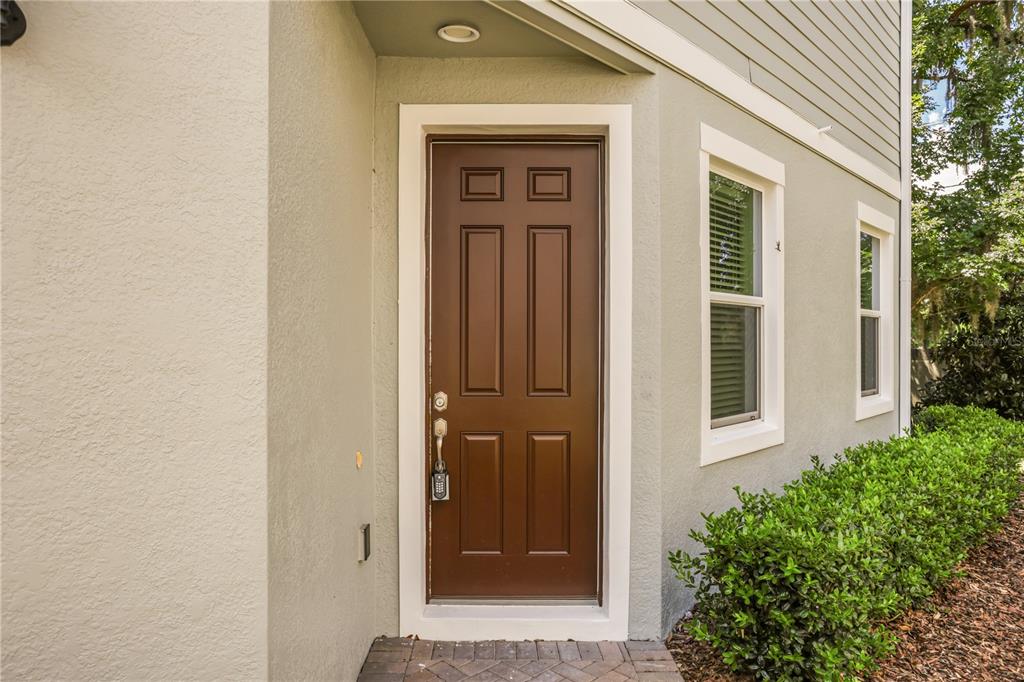 A brown front door with a keypad lock sits on a paved porch by bushes — 2340 BRITWELL PLACE, SANFORD, FL