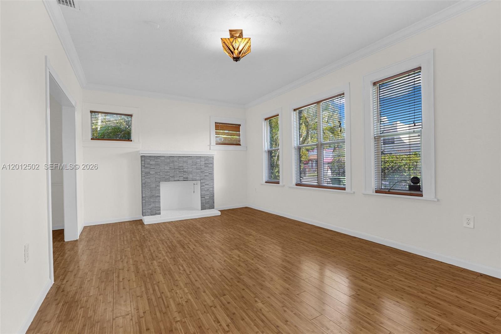 A living room features light wood flooring, white walls, a gray tiled fireplace, and windows — 126 NW 48th St # 0, Miami FL 33127, MIAMI, FL