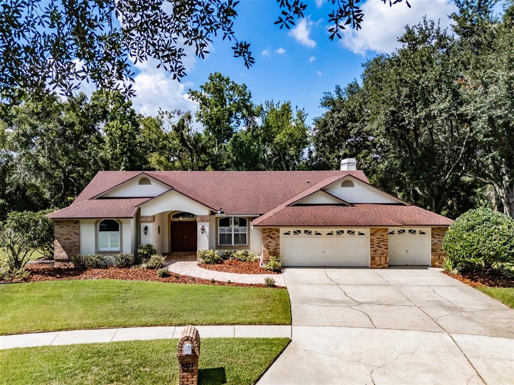 A single-story house with a brown roof, brick accents, and a three-car garage — 507 SURREY LANE, LUTZ, FL