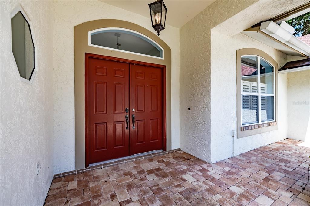 A red double front door with a transom window sits on a brick-paved porch — 507 SURREY LANE, LUTZ, FL