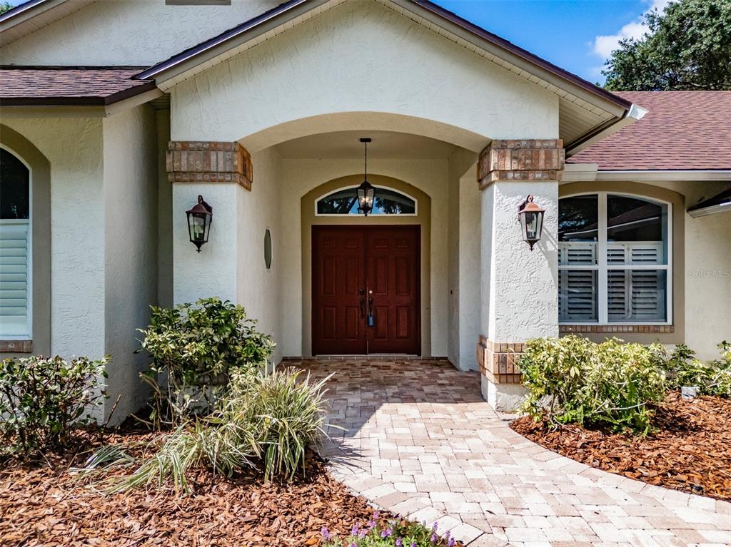 A front entrance with a brick walkway, double wooden doors, and two wall-mounted lanterns — 507 SURREY LANE, LUTZ, FL