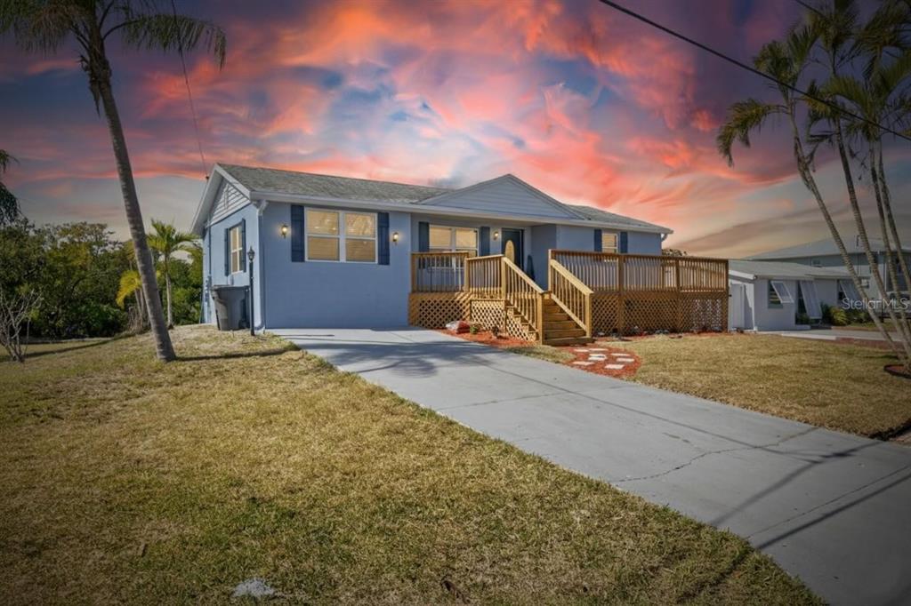 A light blue single-story house features a wooden deck and a concrete driveway at sunset — 827 SEABREEZE DRIVE, RUSKIN, FL