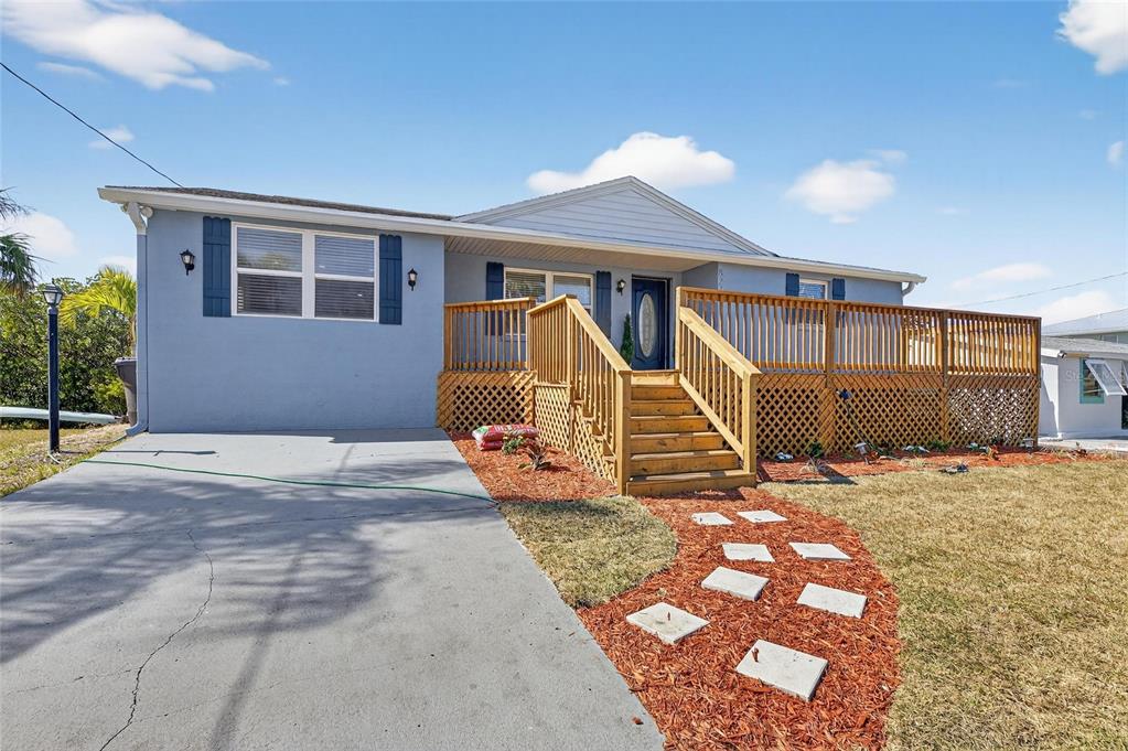 A blue single-story house features a wooden deck, front stairs, and a concrete driveway — 827 SEABREEZE DRIVE, RUSKIN, FL