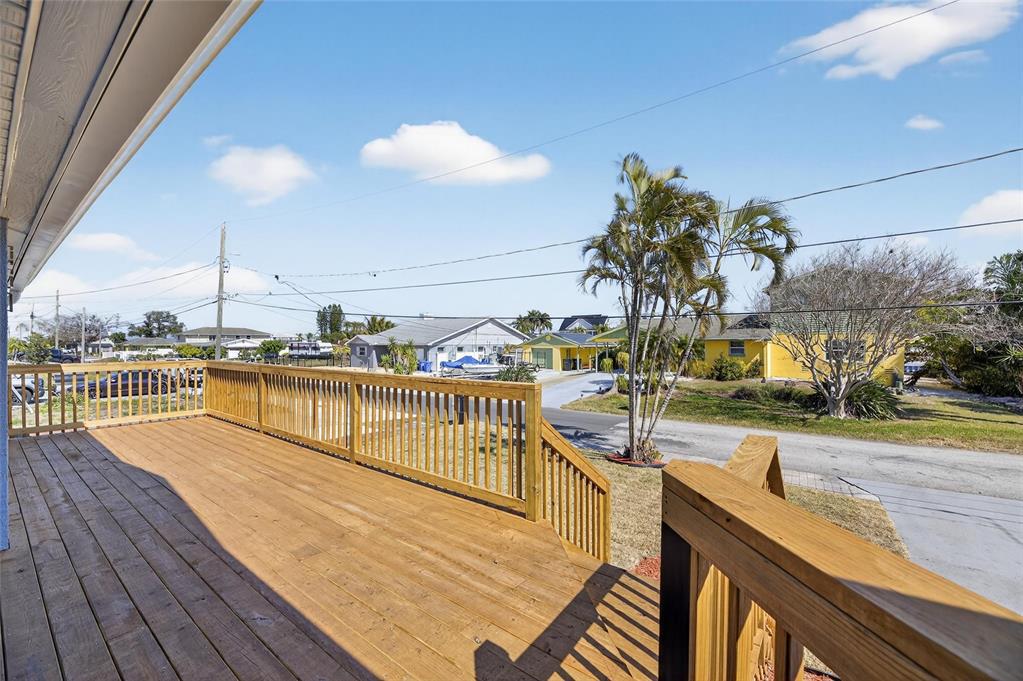 A wooden deck with railings overlooks a residential street with palm trees and houses — 827 SEABREEZE DRIVE, RUSKIN, FL