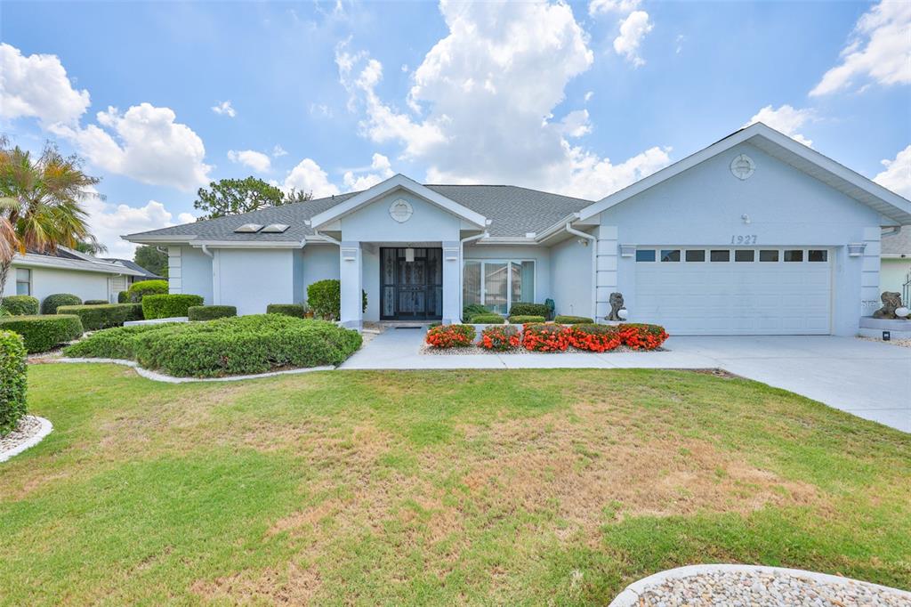 A light blue single-story house features a two-car garage, a front porch, and landscaped gardens — 1927 E VIEW DRIVE, SUN CITY CENTER, FL