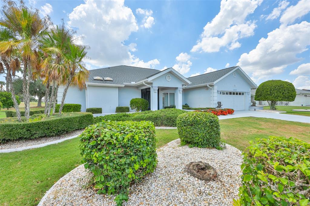 A light blue single-story house with a garage, manicured hedges, and palm trees — 1927 E VIEW DRIVE, SUN CITY CENTER, FL