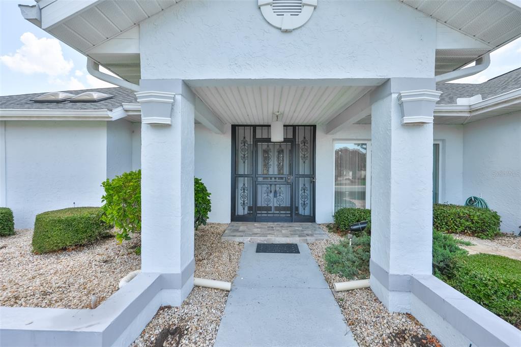 The front entrance of a house features a concrete walkway leading to a dark screen door — 1927 E VIEW DRIVE, SUN CITY CENTER, FL