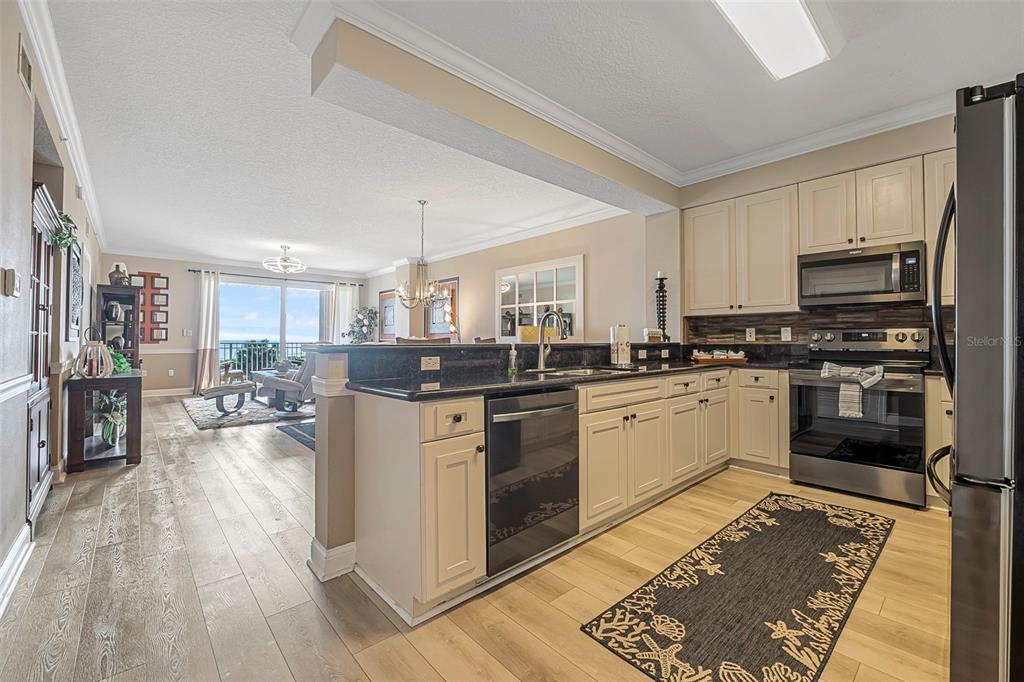 A kitchen with cream cabinets, dark countertops, and stainless steel appliances opens to a living area — 60 SURFVIEW DRIVE UNIT 208, PALM COAST, FL