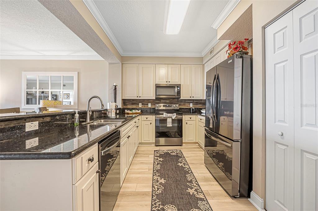 A kitchen with white cabinets, dark granite countertops, stainless steel appliances, and wood-look flooring — 60 SURFVIEW DRIVE UNIT 208, PALM COAST, FL