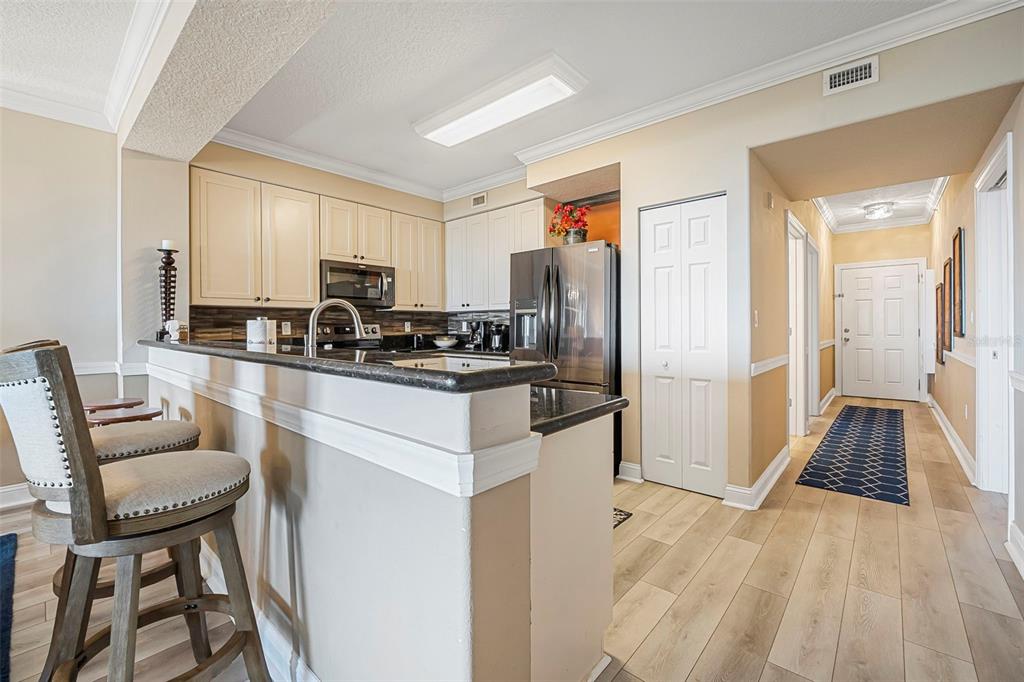 A kitchen with white cabinets, dark countertops, and stainless steel appliances overlooks a hallway — 60 SURFVIEW DRIVE UNIT 208, PALM COAST, FL