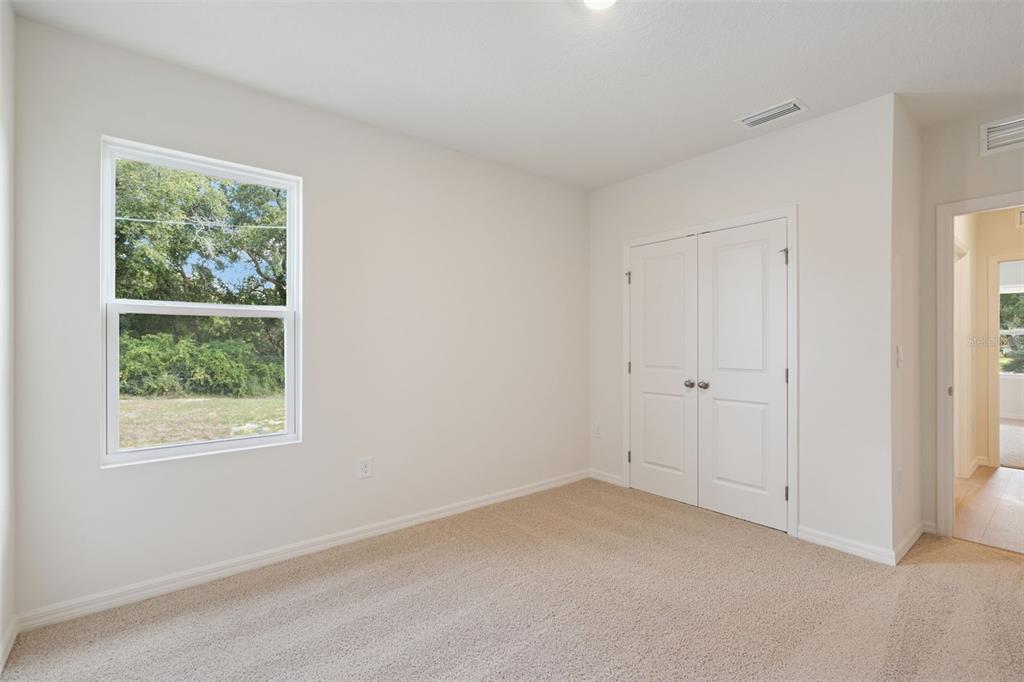 A bedroom with beige carpet, white walls, a window, and double closet doors — 1148 MORFONTAINE STREET, DAYTONA BEACH, FL