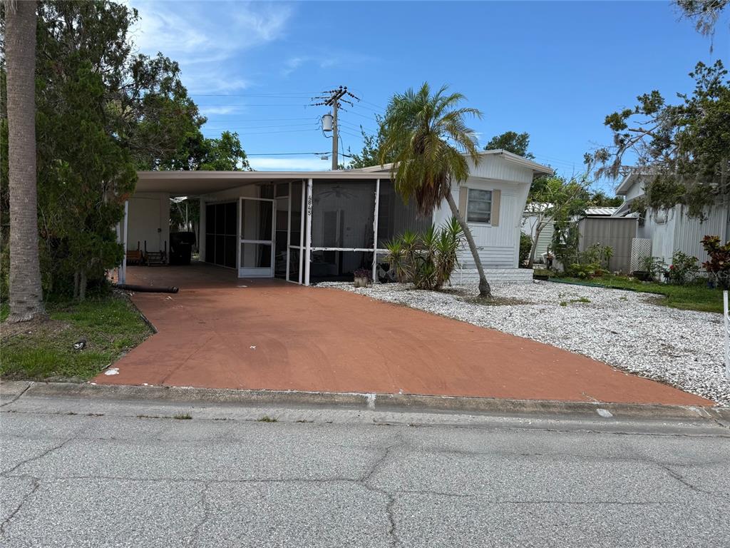 A single-story mobile home features a screened-in porch, a carport, and a gravel front yard — 4845 BOCA RATON AVENUE, SARASOTA, FL
