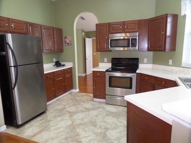 A kitchen features wood cabinets, stainless steel appliances, and white countertops against green walls — 2631 FALLBROOK DRIVE, OVIEDO, FL