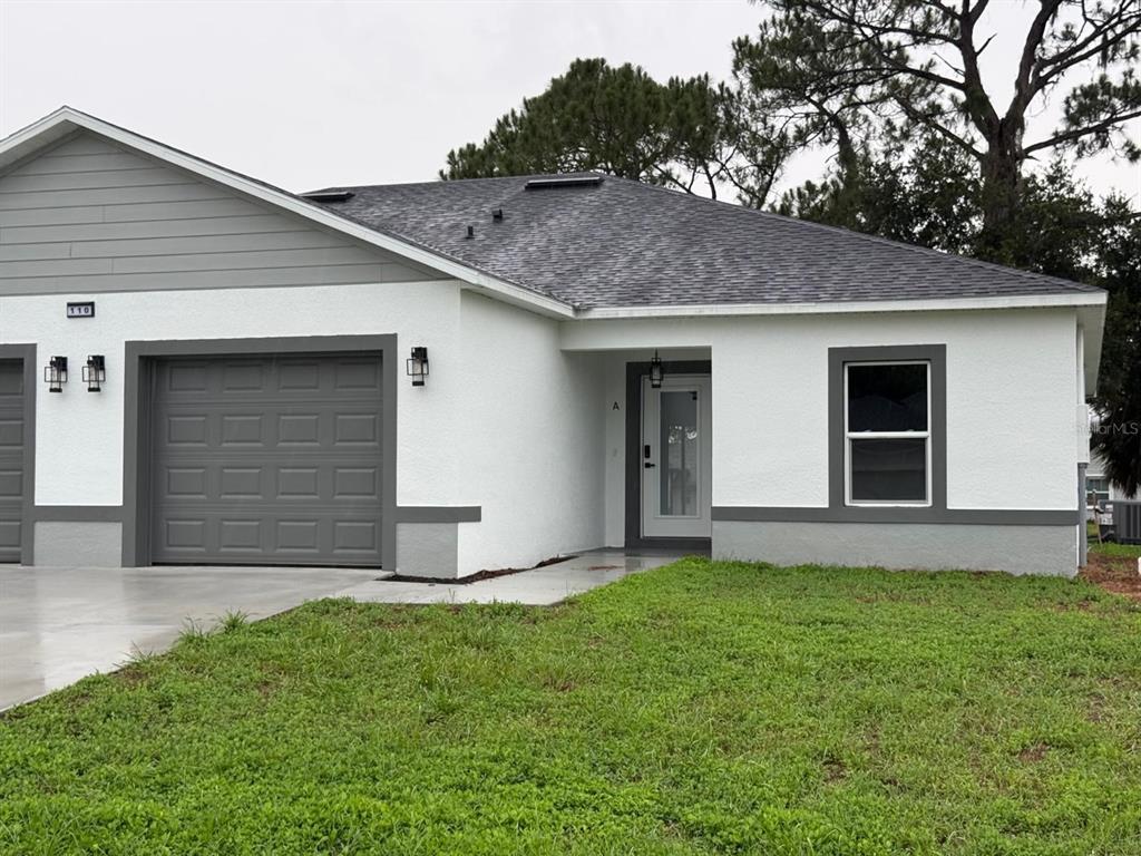 A single-story duplex with white stucco walls, gray trim, a garage, and a front entrance — 110 FRIENDLY CIRCLE UNIT 1, SEBRING, FL
